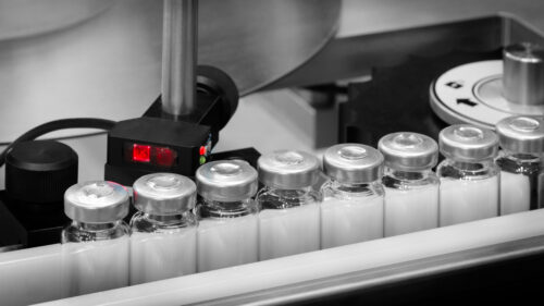Pharmaceutical glass bottles production line Vaccine production in a pharmaceutical factory, conveyor with the glass jars, modern pharmaceutical factory. Closeup of ampules are being filled with vaccine